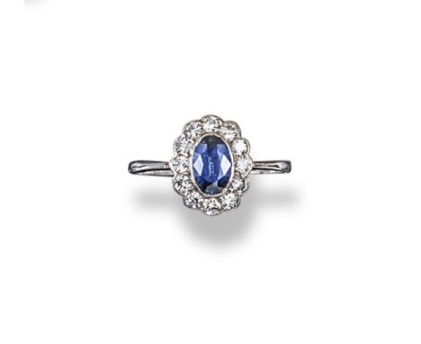 A sapphire and diamond cluster ring, the oval-shaped sapphire is set within a surround of circular-cut diamonds in platinum. 