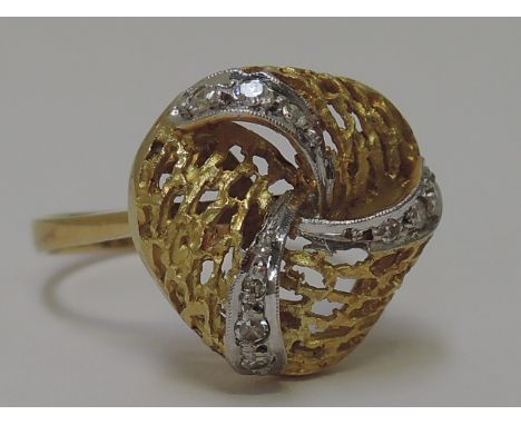 A yellow metal dress ring having a stylised knot with diamond chip decoration on a yellow metal loop bearing continental mark