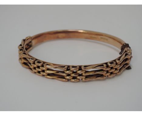 A cased Victorian yellow metal hinged bangle having gate bracelet style decoration to the front, stamped 9ct Full, 