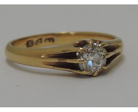 A diamond solitaire ring in a heavy claw setting within raised ridged shoulders on an 18ct gold loop