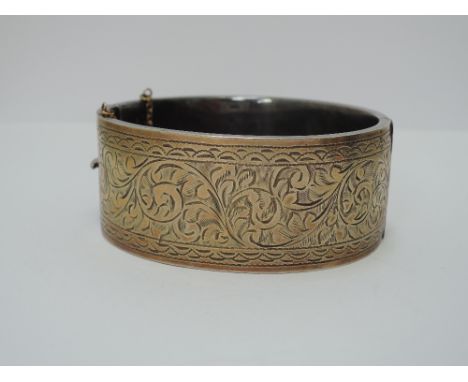 A white metal hinged bangle having yellow metal overlay to engraving, stamped silver & 9ct gold front
