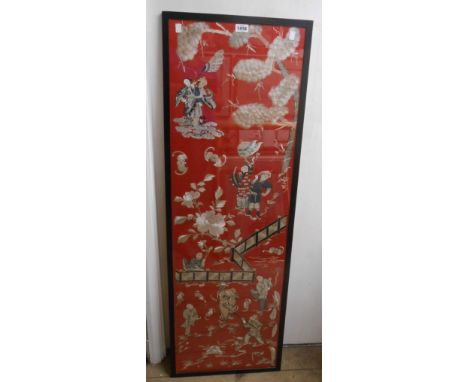 A framed 20th Century Chinese embroidery panel with figures, fence and flowers on red ground - 1.25m X 40cm
