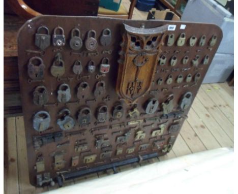 A wooden display board containing a large quantity of antique and vintage padlocks, bolts, locks and keys with a central carv