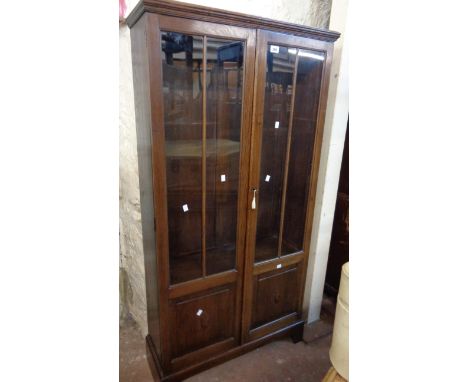 An 80cm early 20th Century stained oak book cabinet with shelves enclosed by a pair of part glazed panel doors, set on bracke