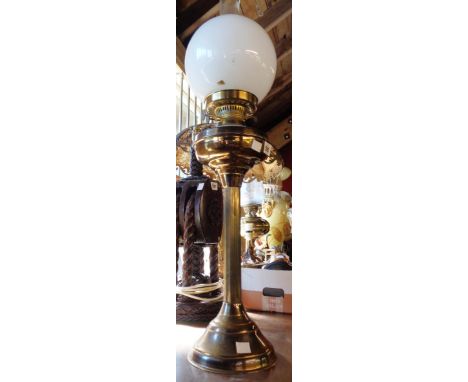 A brass oil lamp of Corinthian column form with double burner, clear glass chimney and white opaque glass globe shade