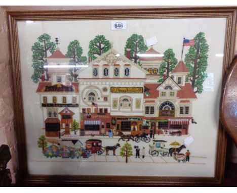 A US wood framed embroidery panel depicting an American street scene with shop fronts and horses pulling carts