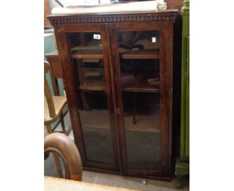 A 70cm early 20th Century stained wood book cabinet with dentil moulding and shelves enclosed by a pair of glazed panel doors