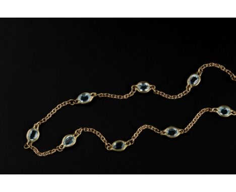 A BLUE TOPAZ SET LONG CHAIN, the 9ct gold trace-link chain spaced by spectacle set oval mixed-cut blue topaz, length 67cm
