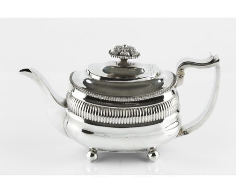 A GEORGE III SILVER TEAPOT, of rounded rectangular outline with gadrooned borders, foliate knop, shaped handle and on ball fe