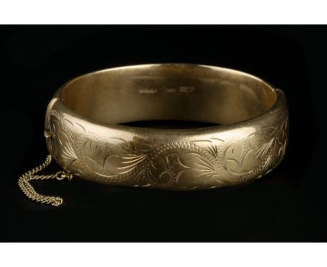 A 9CT GOLD BANGLE, of hinged oval form, with foliate engraved decoration, inner diameter 6.2cm