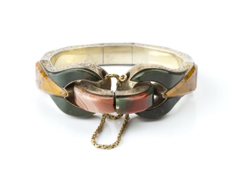 A VICTORIAN HARDSTONE BANGLE, of hinged oval form with foliate scroll engraved decoration, inlaid with vari-coloured agate an