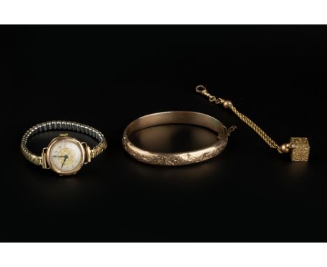 A LATE VICTORIAN 9CT GOLD BANGLE, of hinged oval form, with engraved decoration, a ropetwist-link chain section, suspending a