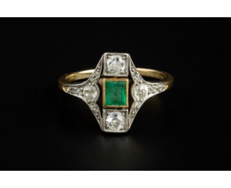 AN EMERALD AND DIAMOND PANEL RING, circa 1915-25, the lozenge-shaped panel centred with a rectangular step-cut emerald betwee