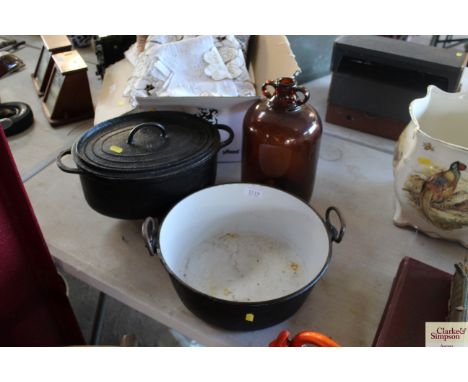 An enamel preserve pan, an oval cast iron casserole on legs and a brown glass demi-john