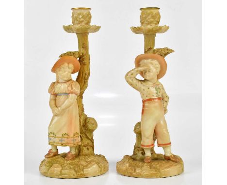 ROYAL WORCESTER; a pair of blush ivory figural candle holders, a boy and girl standing beside tree, numbered 1141 to the unde