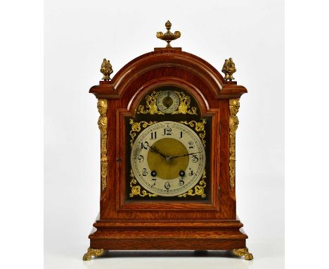 An early 20th century oak mantel clock with applied brass urn finial and four further scrolling urn finials above the brass f