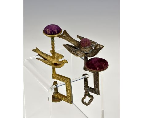 Two Hummingbird sewing clamps, both with rectangular foliate decorated frames below pin cushions, one in gilt metal, the othe