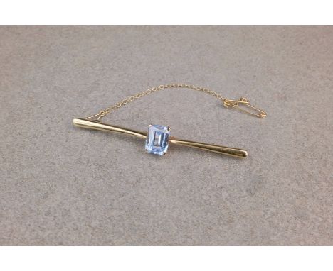 A 9ct gold and aquamarine bar brooch, featuring an emerald cut aquamarine to the centre measuring approximately 9x7mm and hel