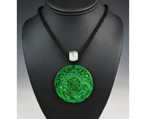 A carved apple green jade pendant on black cord, with carved foliate detailing, measuring approximately 55mm in diameter and 