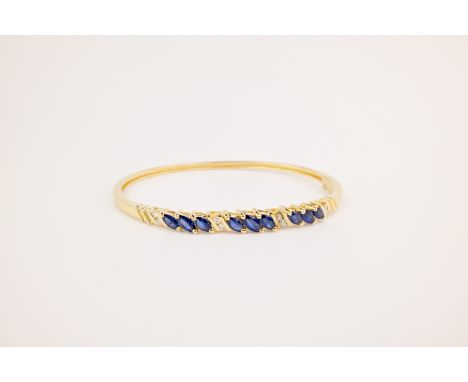 A 14ct gold, blue sapphire and diamond bangle, the polished, hinged bangle studded with trios of marquise cut sapphires and p