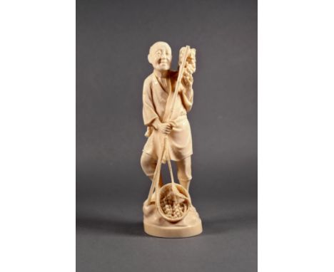 A Japanese carved ivory okimono of a farmer, Meiji period (1868-1912), the man standing on rocky ground, holding a bunch of g