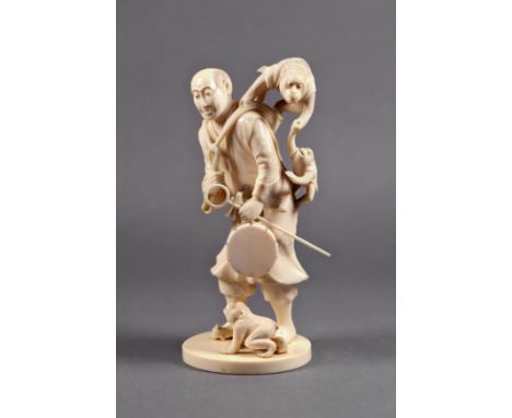 A Japanese carved ivory okimono of a performer, Meiji period (1868-1912), the man with a drum in one hand, two monkeys on his