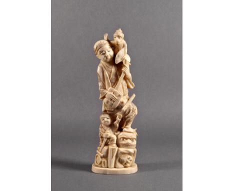 A Japanese carved ivory okimono of a musician, Meiji period (1868-1912), standing with a monkey on his shoulder, one foot on 