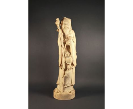 A Chinese carved ivory figure of Shou Lao, the smiling figure holding a long, knarled staff, in the other hand he holds a bas