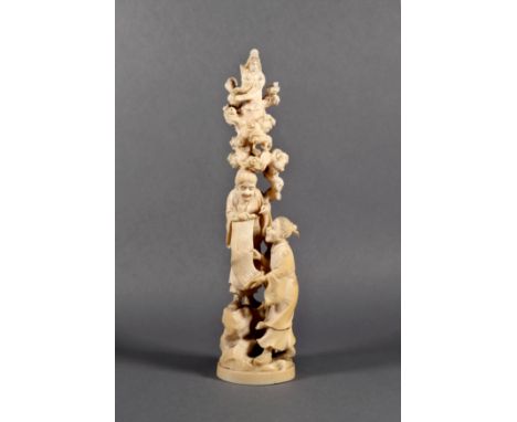 A Chinese ivory carving of two figures holding a scroll, Qing Dynasty, standing on rocks with Guanyin standing amidst clouds 