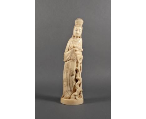 A Chinese carved ivory figure of a noblewoman, Qing Dynasty, dressed in flowing robes and resting one arm on a tall stump of 