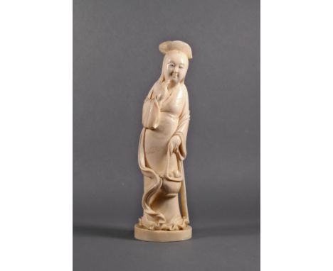 A Japanese carved ivory okimono of a lady, Meiji period (1868-1912), standing with a basket of peaches in one hand and the ot