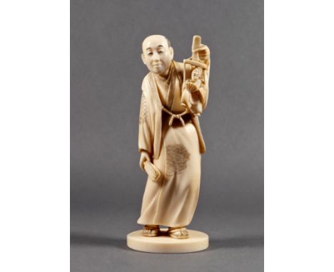 A Japanese carved ivory okimono of a puppeteer, Meiji period (1868-1912), holding a wooden frame from which hangs a miniature