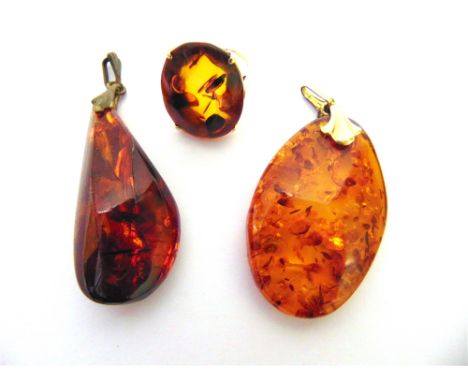 AN AMBER RING stamped '14k', the oval panel approximately 23mm by 16mm; and two amber pendants; 21g gross
