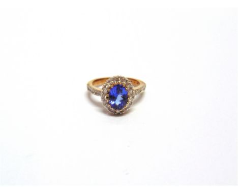 A 9 CARAT GOLD TANZANITE AND DIAMOND CLUSTER RING the oval cut stone enclosed by sixteen small brilliant cuts and six single 