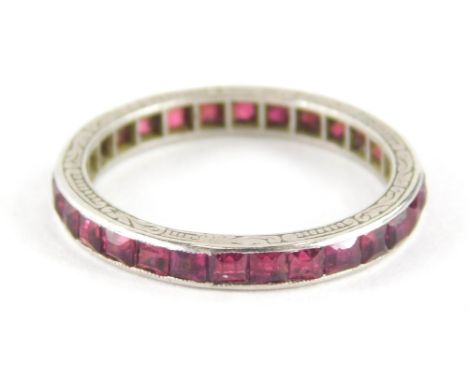 A ruby eternity ring, set with square cut rubies, on a white metal outer bordering with scroll detailing rubbed, unmarked, ri