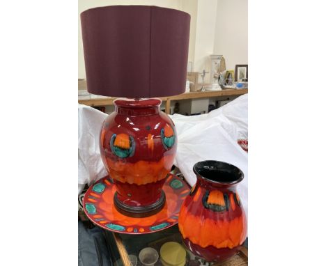 A large Poole pottery table lamp together with a similar charger and vase in reds and oranges 