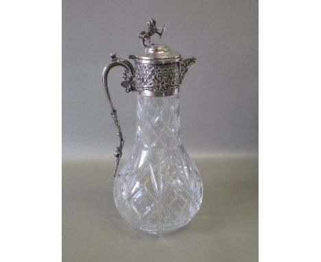 LARGE CUT GLASS CLARET JUG WITH A SILVER PLATED NECK WITH FLORAL DECORATION, THE HINGED COVER WITH LION FINIAL HOLDING A SHIE