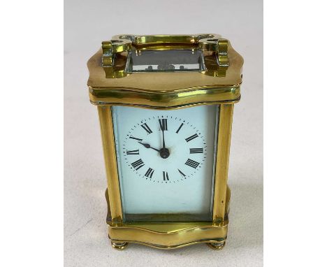 An early 20th century French brass carriage clock with serpentine outlined mounts and Roman numerals to the white enamel dial