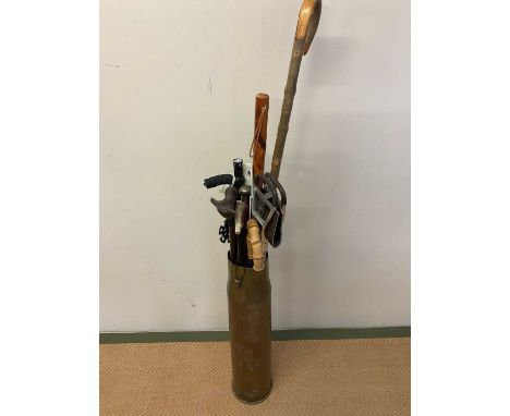 A large brass shell case and a small group of walking sticks and canes including a shooting stick.
