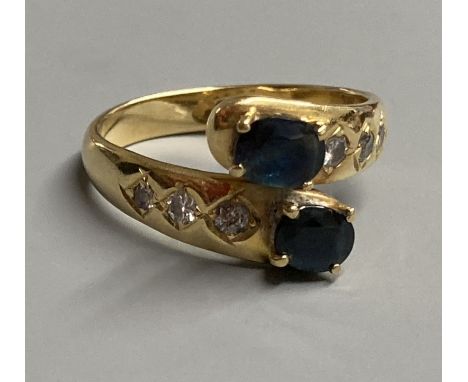 A modern 18ct and two stone sapphire crossover ring, with diamond set shoulders, size P, gross 5.4 grams.