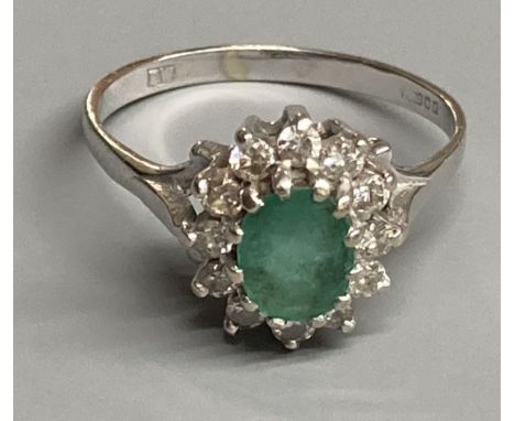 A modern 18ct white gold, emerald and diamond set oval cluster ring, size O/P, gross 3.6 grams.