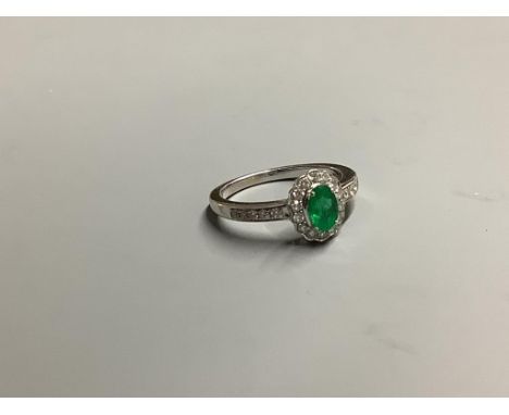 A modern 18ct white gold, emerald and diamond set oval cluster ring, with diamond set shoulders, size L, gross weight 3.4 gra