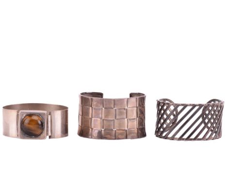A tiger's eye bangle and two cuff bracelets; the bangle with a tension clamp opening, set with a round tiger's eye cabochon, 