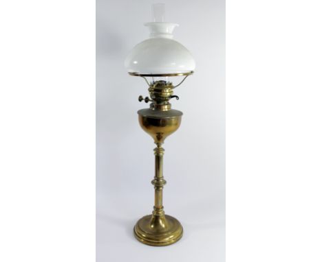 An early 20th century English brass oil lamp with white opal glass shade and glass chimney, standing on a brass column with s