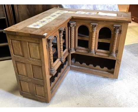 An Early 20th century oak corner bar of architectural form, the top later inset with tiles, over two arcaded doors with appli