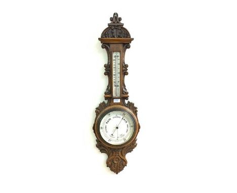 A Late Victorian aneroid barometer and thermometer in an oak floral and scroll carved banjo pattern case, with white ceramic 