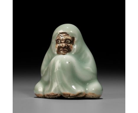 A CELADON GLAZED PORCELAIN NETSUKE OF DARUMAUnsignedJapan, Kyoto, 19th centuryThe patriarch of Zen Buddhism seated enveloped 