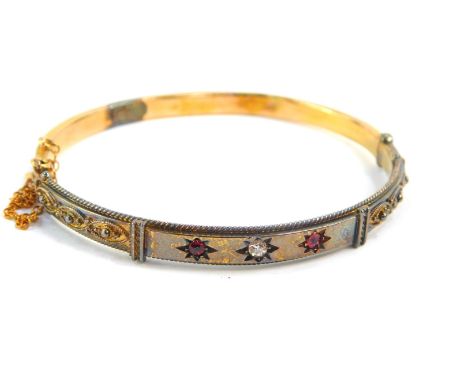 A 15ct gold bangle set, with a diamond flanked by a pair of spinnels, safety chain as fitted, 8.2g.