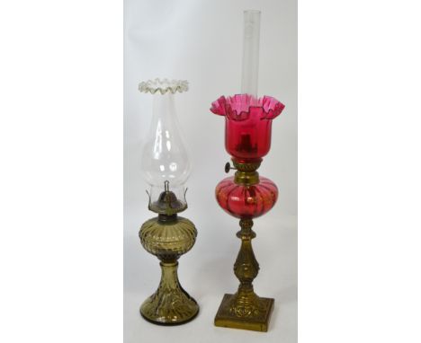 A brass oil lamp with cranberry glass font and shade, height 56cm and a similar smaller example with clear glass chimney, hei
