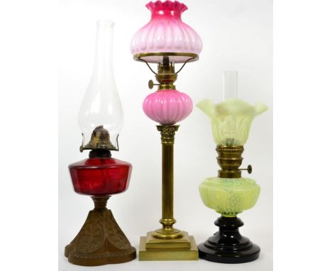 Three oil lamps comprising a cranberry glass gilt metal oil lamp, a yellow vaseline reservoir and shade oil lamp and a brass 